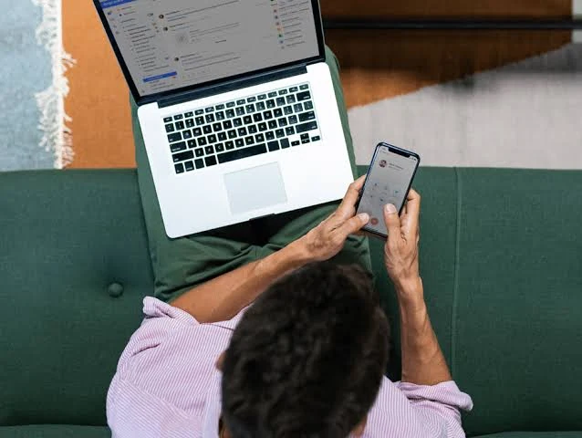 Professional using smartphone and laptop to communicate with clients
